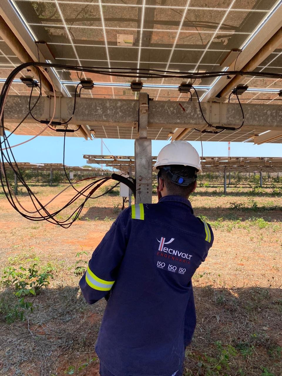 Técnico da Tecnvolt Engenharia trabalhando no cabeamento de strings sob os módulos fotovoltaicos